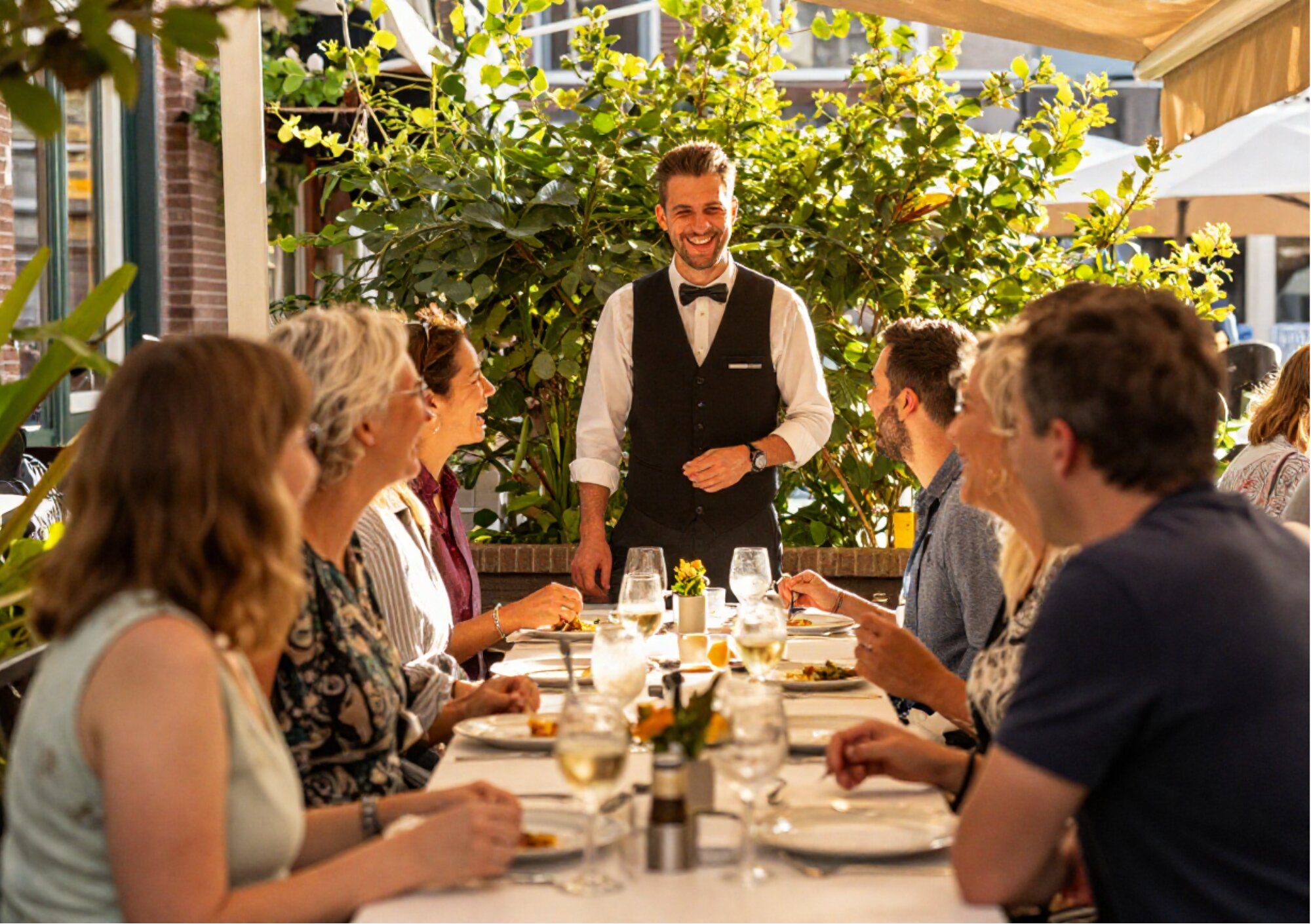 Lachende ober verwelkomt gasten aan een gedekte tafel op een terras