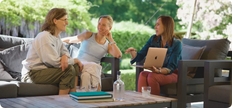 Aanstaand bruidspaar in gesprek met een locatiemanager tijdens een ontspannen vervolgafspraak in de tuin